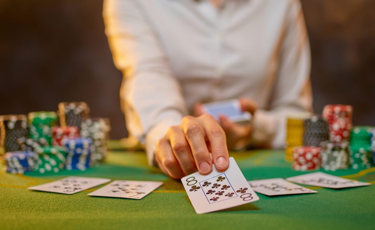 A hand holds a poker card over a green poker table.